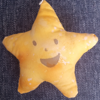 A yellow five pointed plushie star with a happy face on it