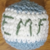 A crochet planet with blue caps and a white band around the middle. It has "EMF" embroidered on it in green.