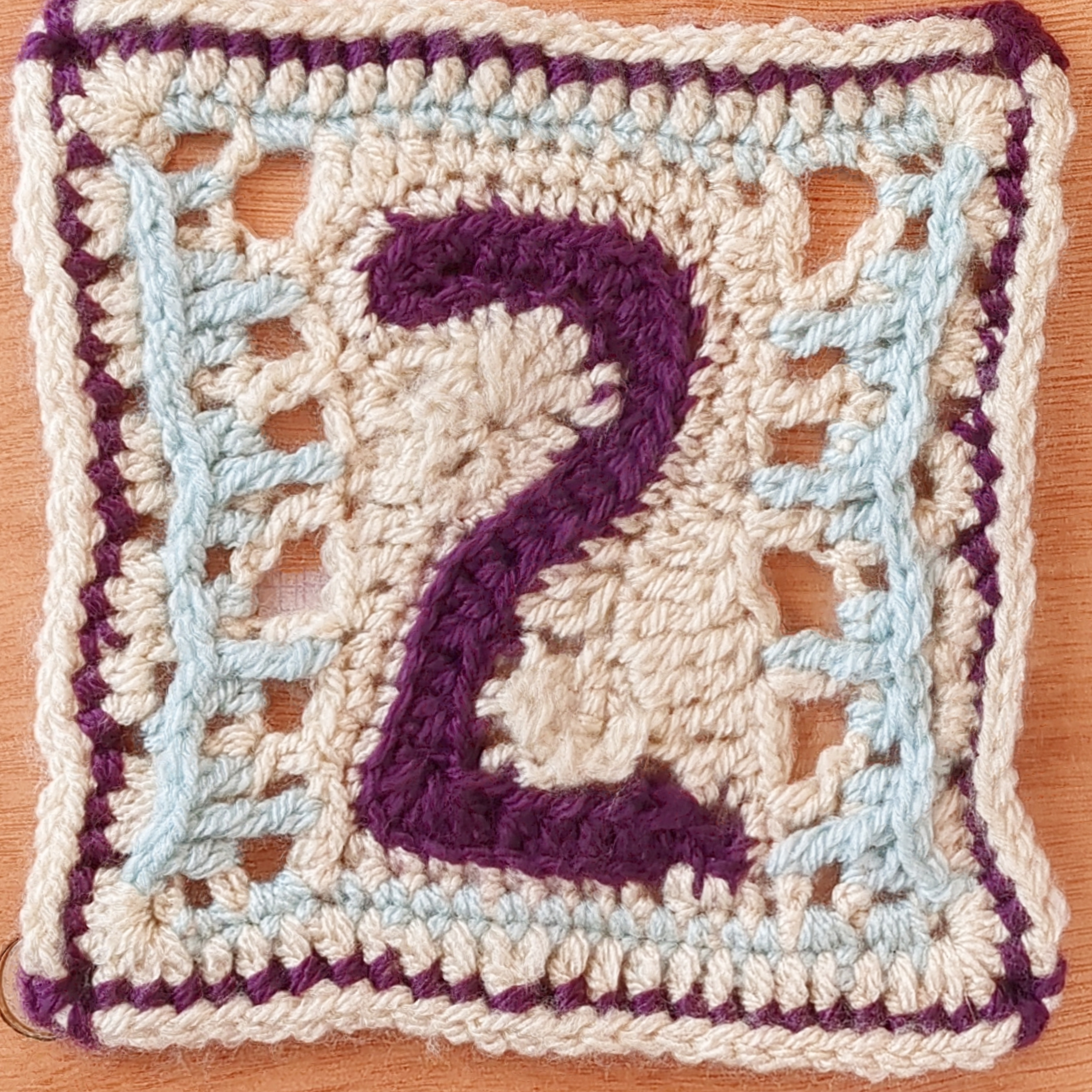 Purple, white, and light blue crochet square showing the number 2 in the centre