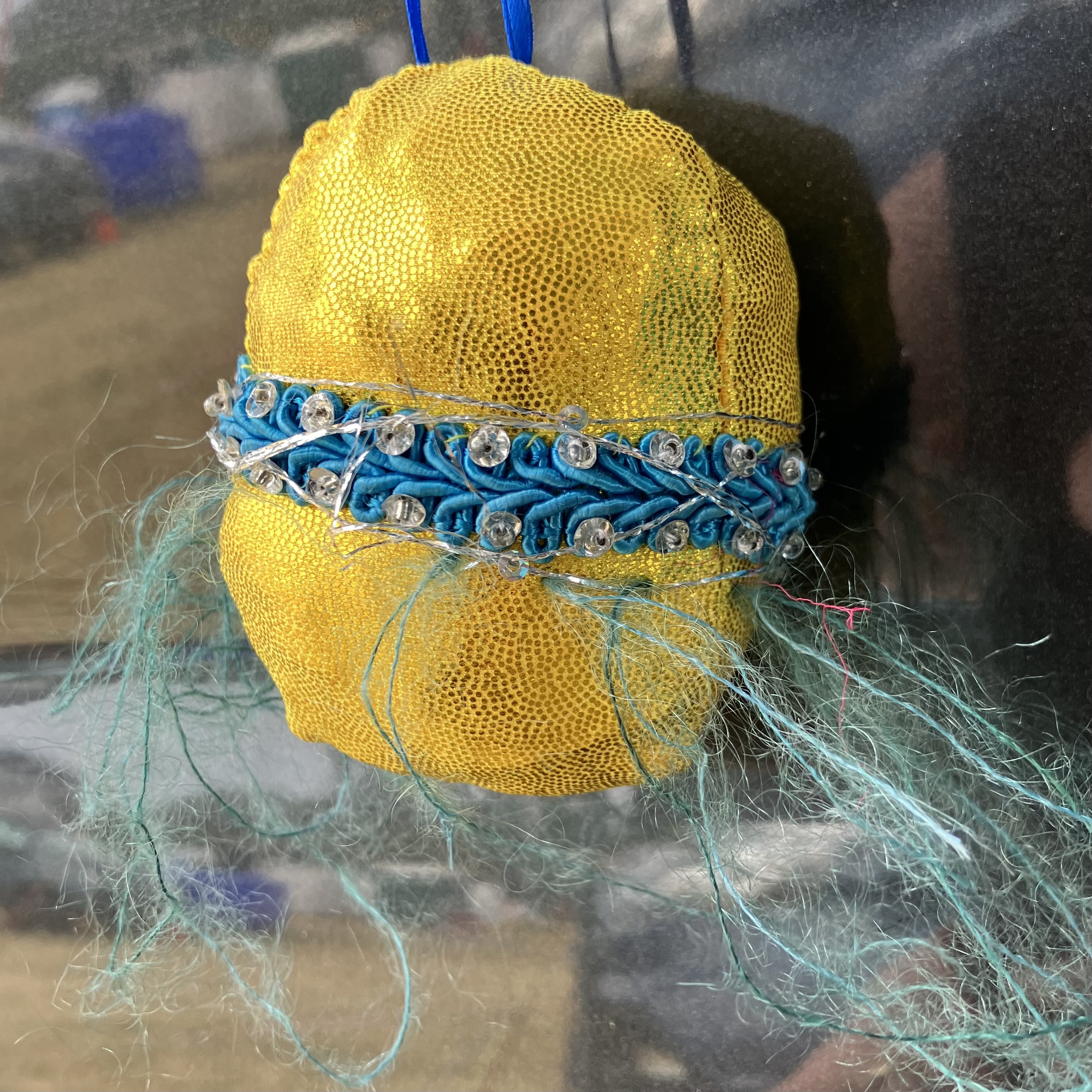 Yellow planet with a blue belt & some silver sequins around the middle & some green mohair (fluffy) yarn trailing from it.