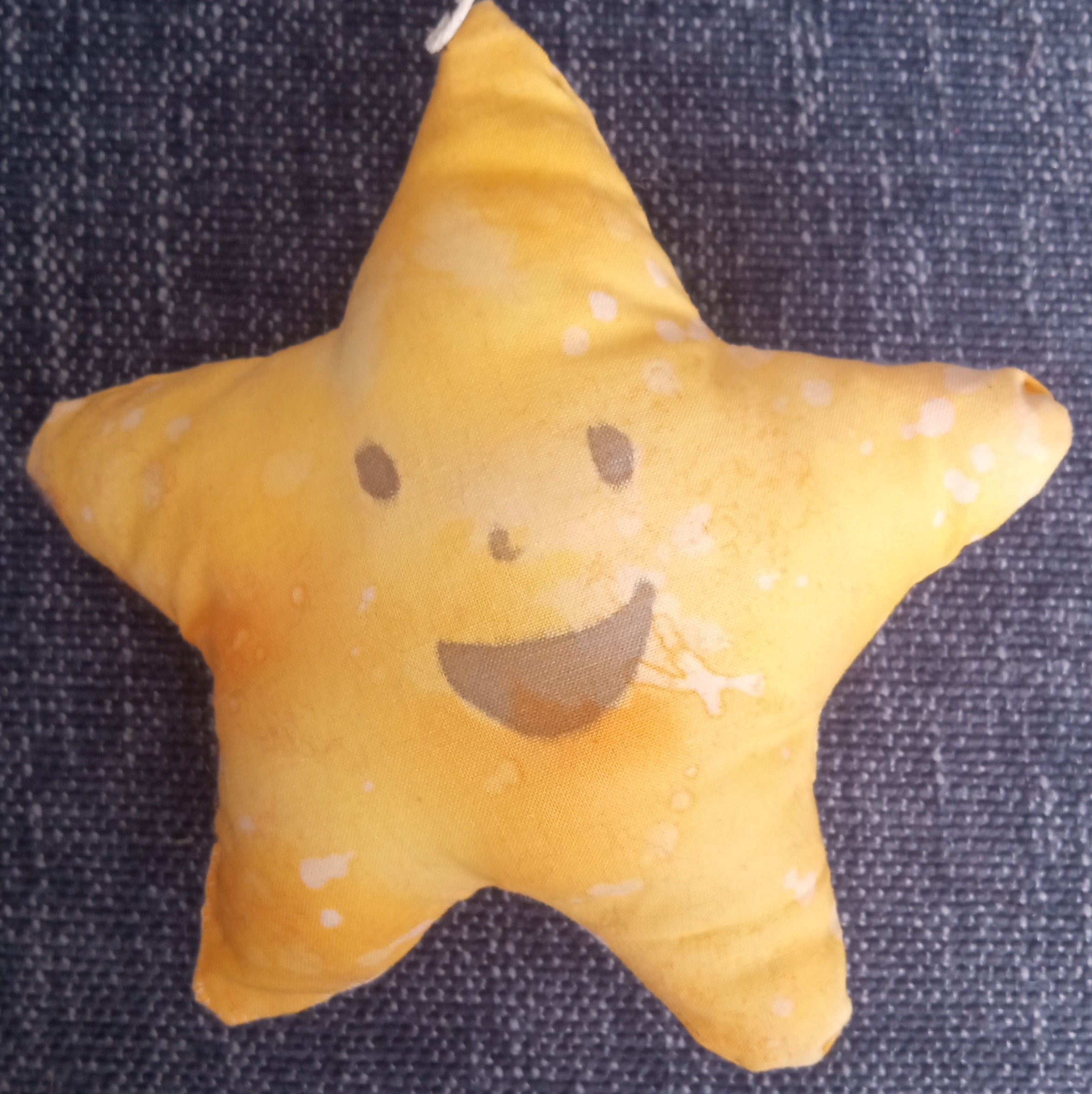 A yellow five pointed plushie star with a happy face on it